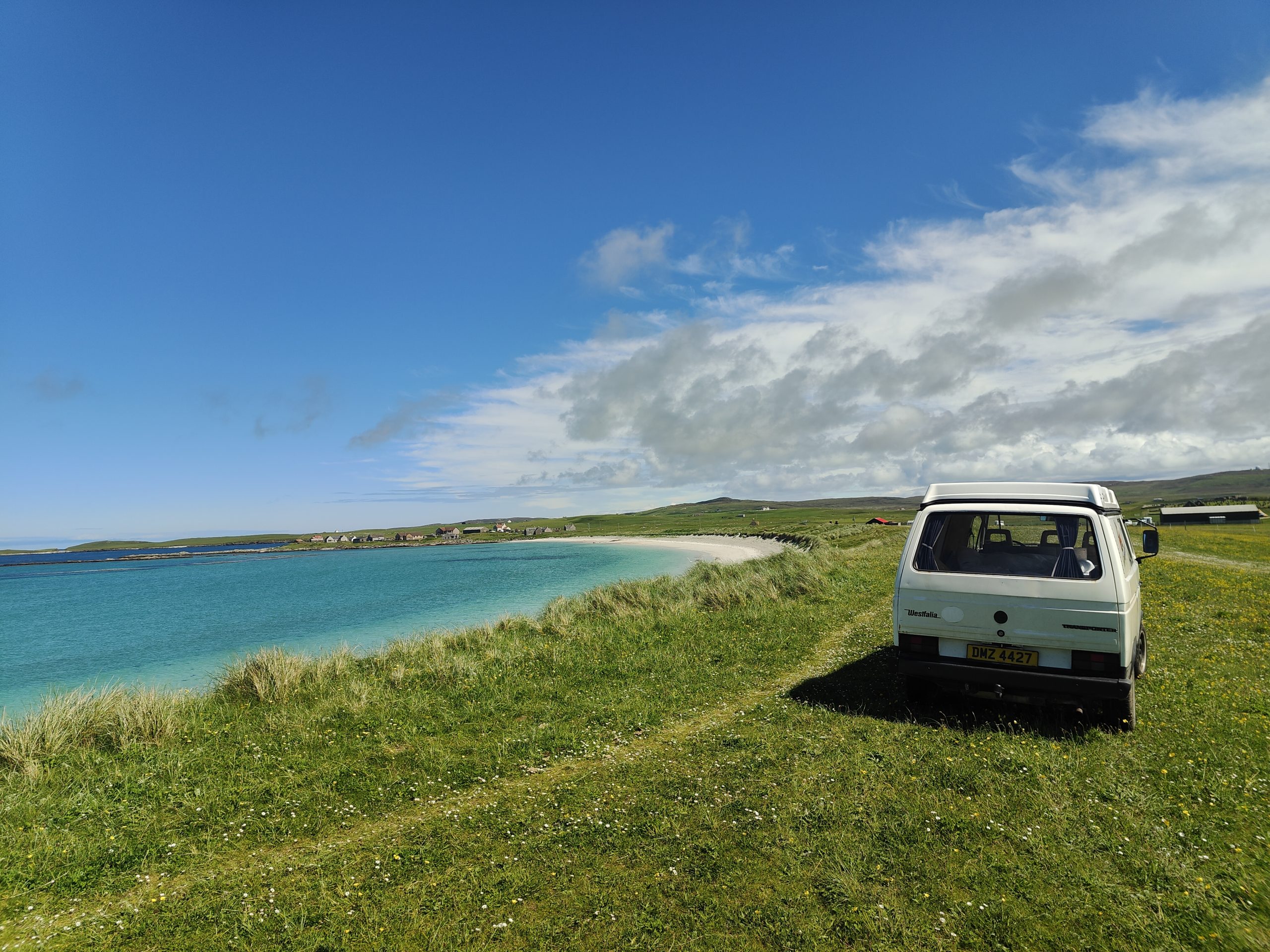 my elderly volkswagen van parked on a green field by the sea under a brilliant blue sky